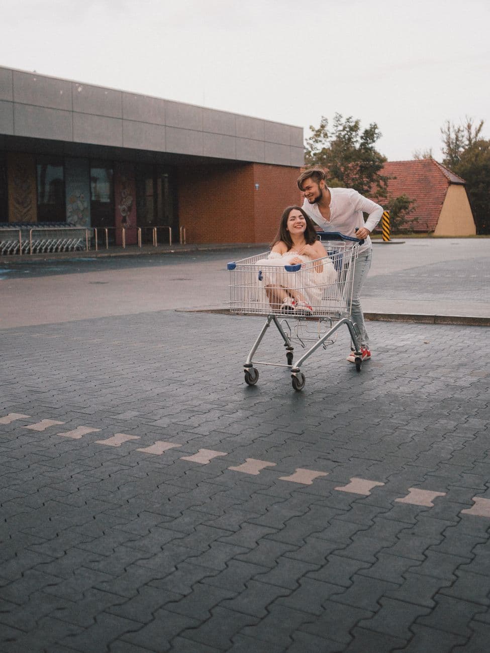 Two adults enjoying a fun ride in a shopping cart outside a mall.