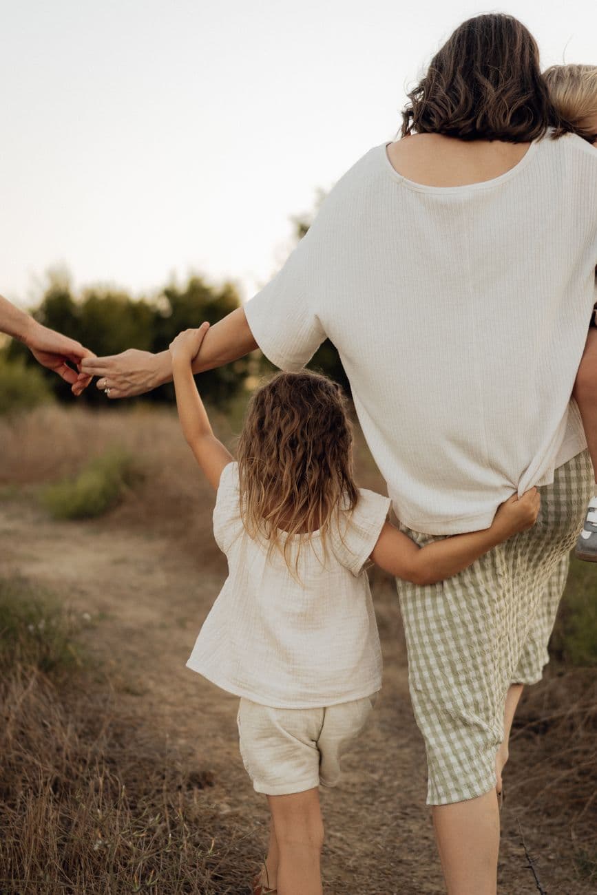 A mother and child walking outdoors, holding hands on a scenic path.