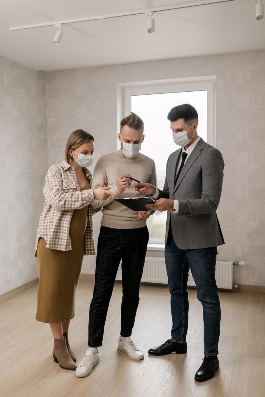 Couple signing real estate documents with a real estate agent in a new home while wearing masks.