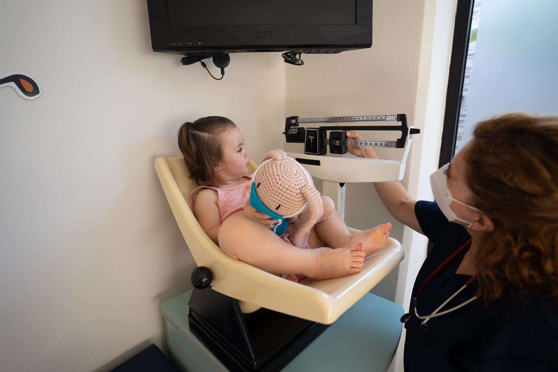 A young girl being weighed by a nurse in a pediatric examination room.
