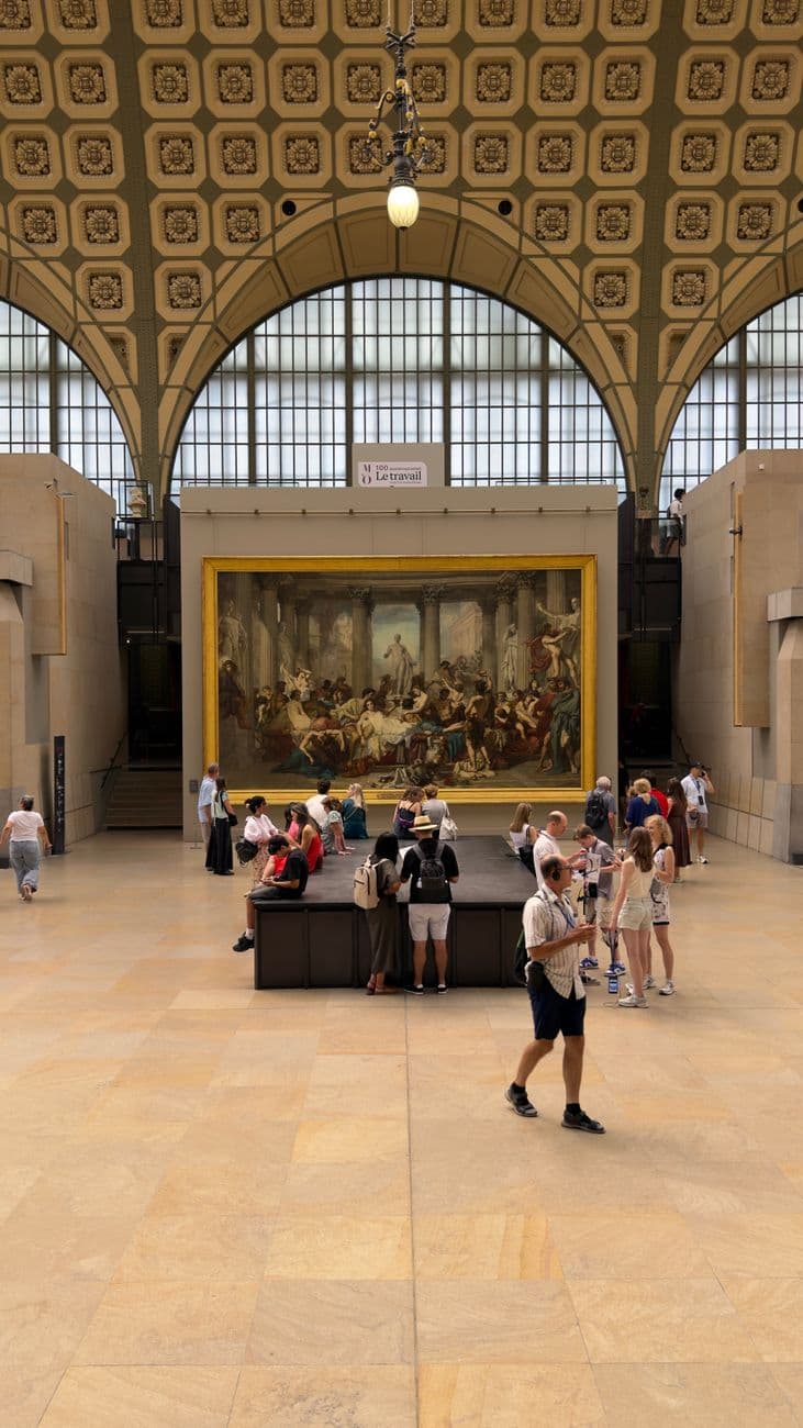 Visitors explore artwork in the iconic Musée d'Orsay, Paris, under an ornate ceiling.
