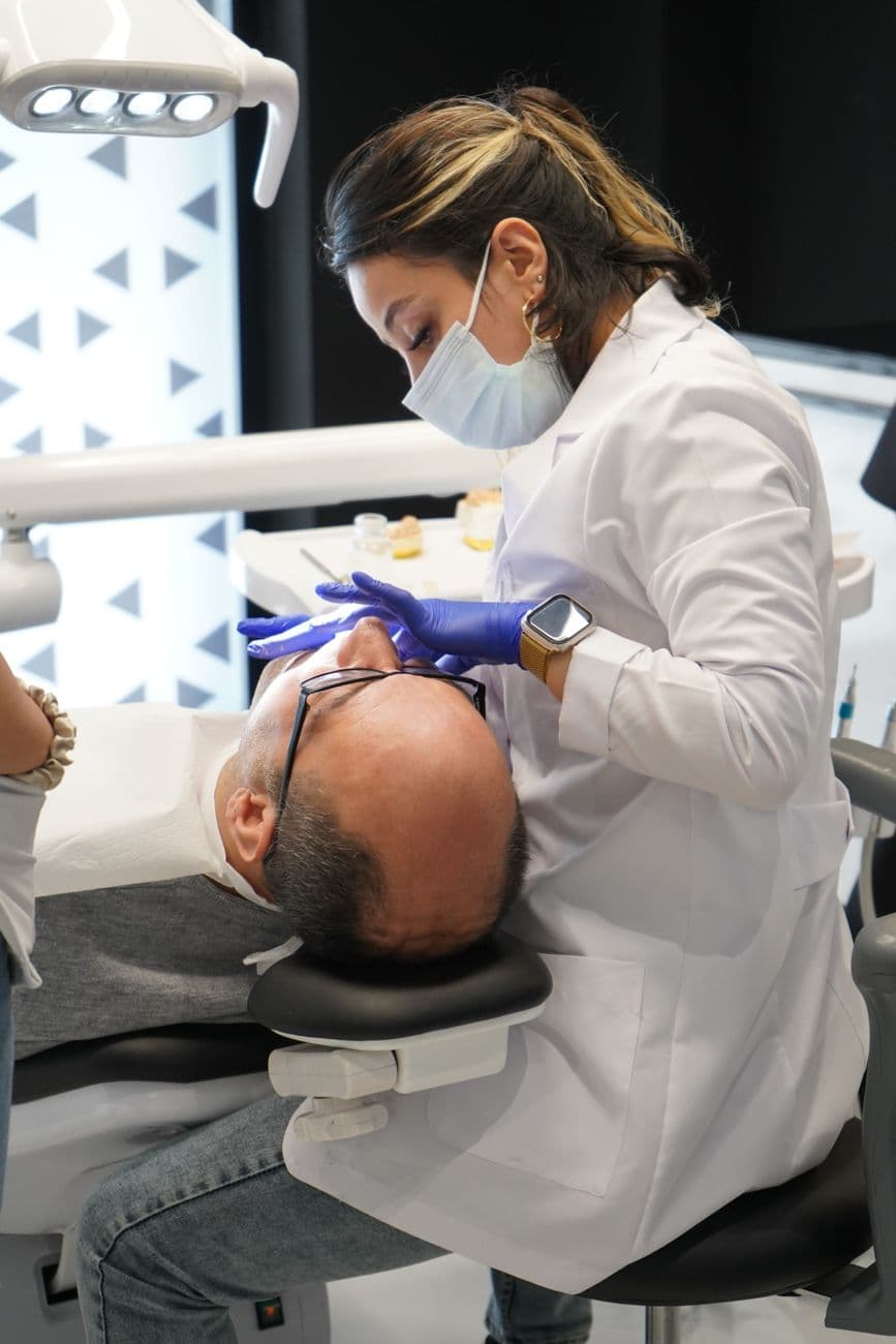 Dentist in white coat examining a patient's teeth in a modern clinic setting.