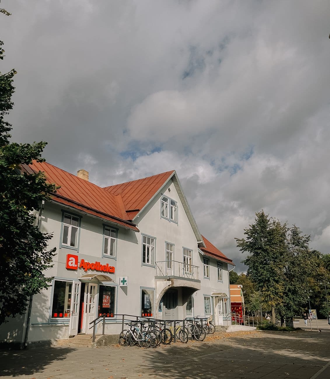 A quaint European pharmacy with bicycles parked outside under a cloudy summer sky.