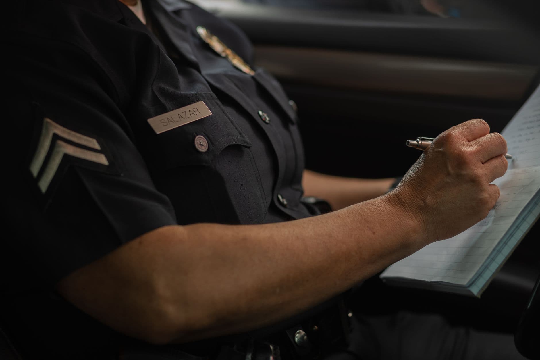 Close-up of a police officer writing in a notebook while sitting in a car, focused detail.