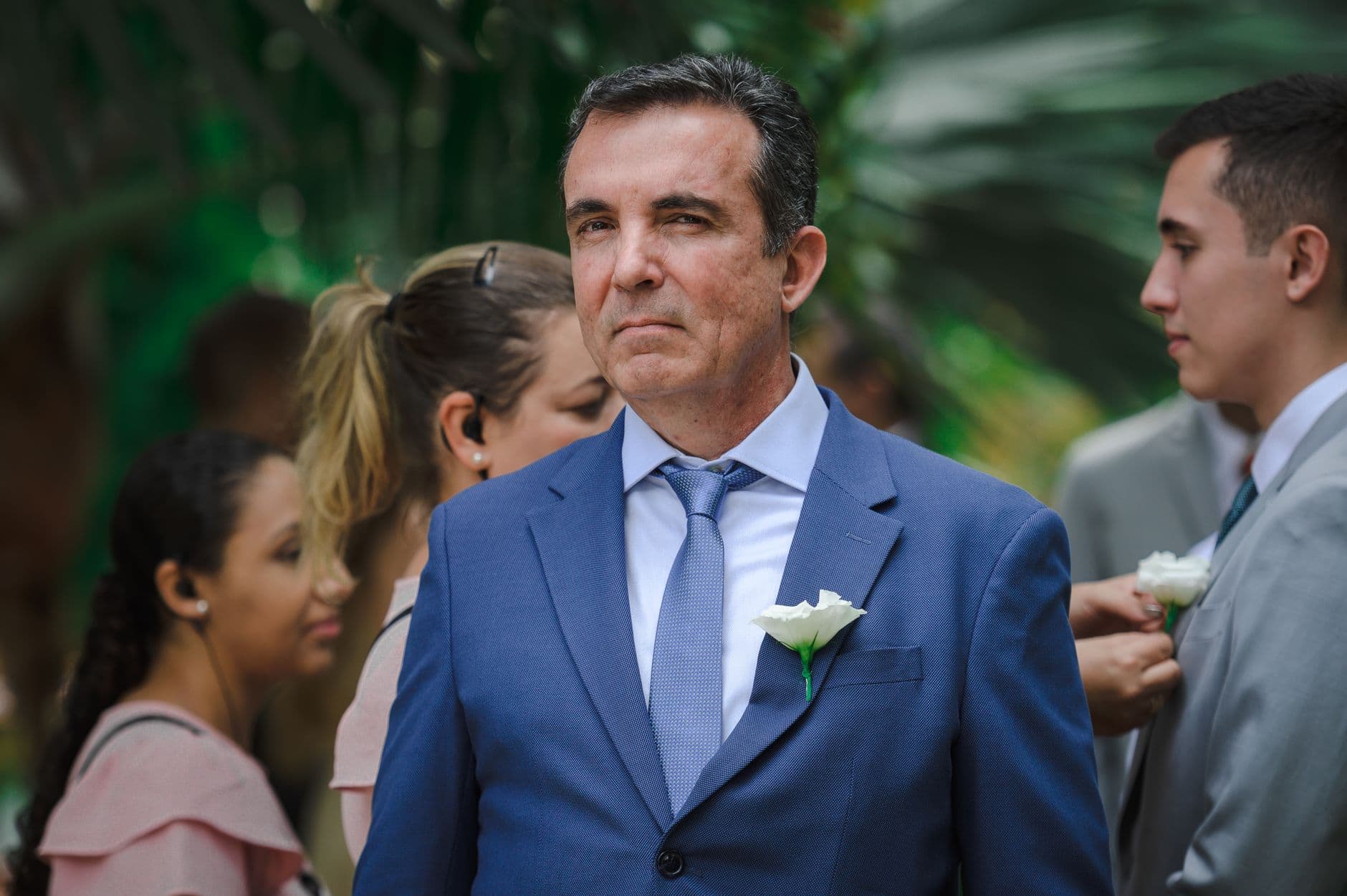 Portrait of an elegant man in a blue suit with boutonniere at an outdoor wedding ceremony.