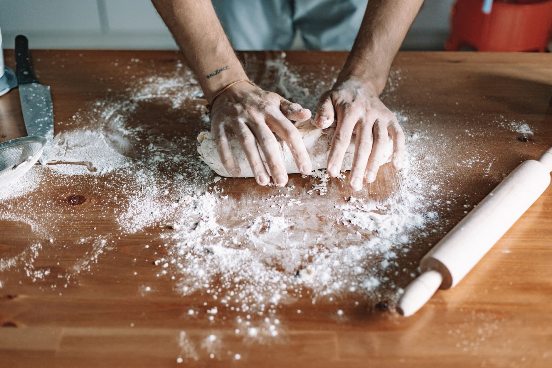 Hands kneading dough with flour on a wooden table, showcasing food preparation.