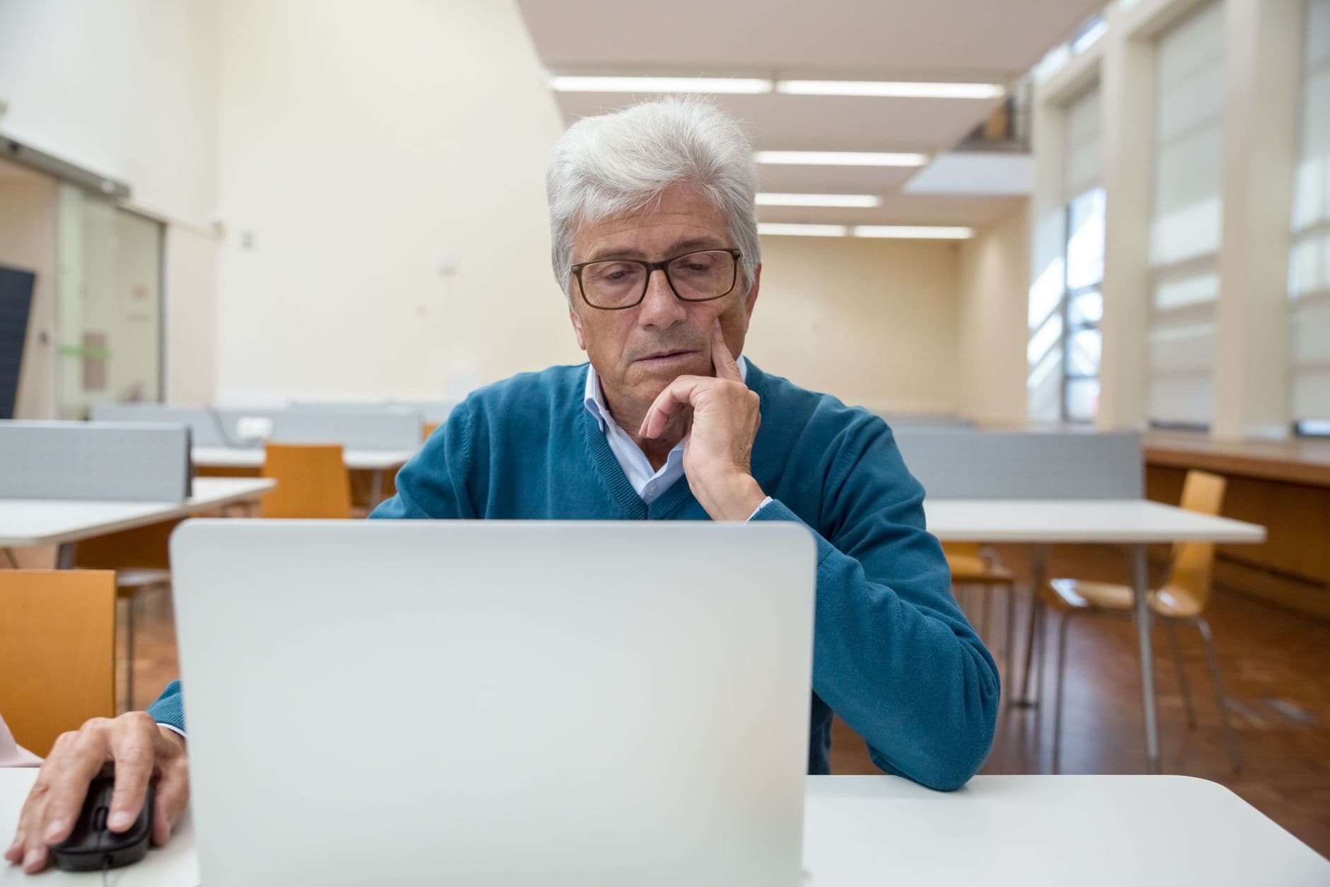Mature man focused on laptop work in a contemporary library setting.