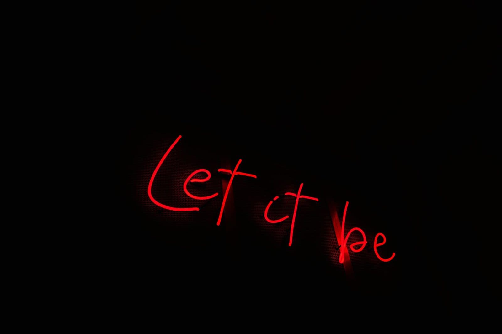 Image of 'Let it be' in vibrant red neon text on a dark background, conveying tranquility.