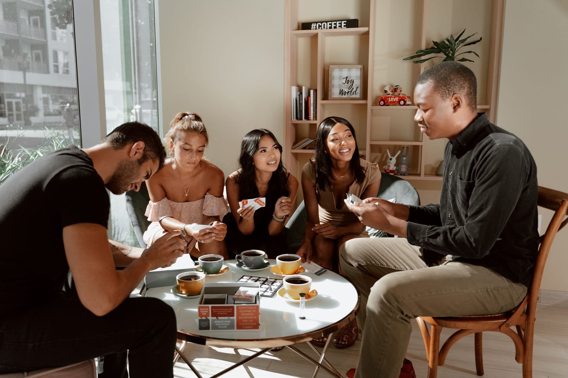 Group of diverse friends playing board games in a cozy café setting, enjoying coffee together.