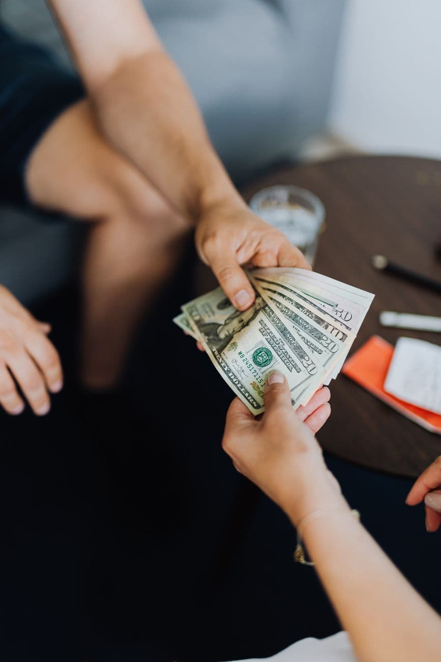 A close-up view of hands exchanging dollar bills indoors, symbolizing payment.