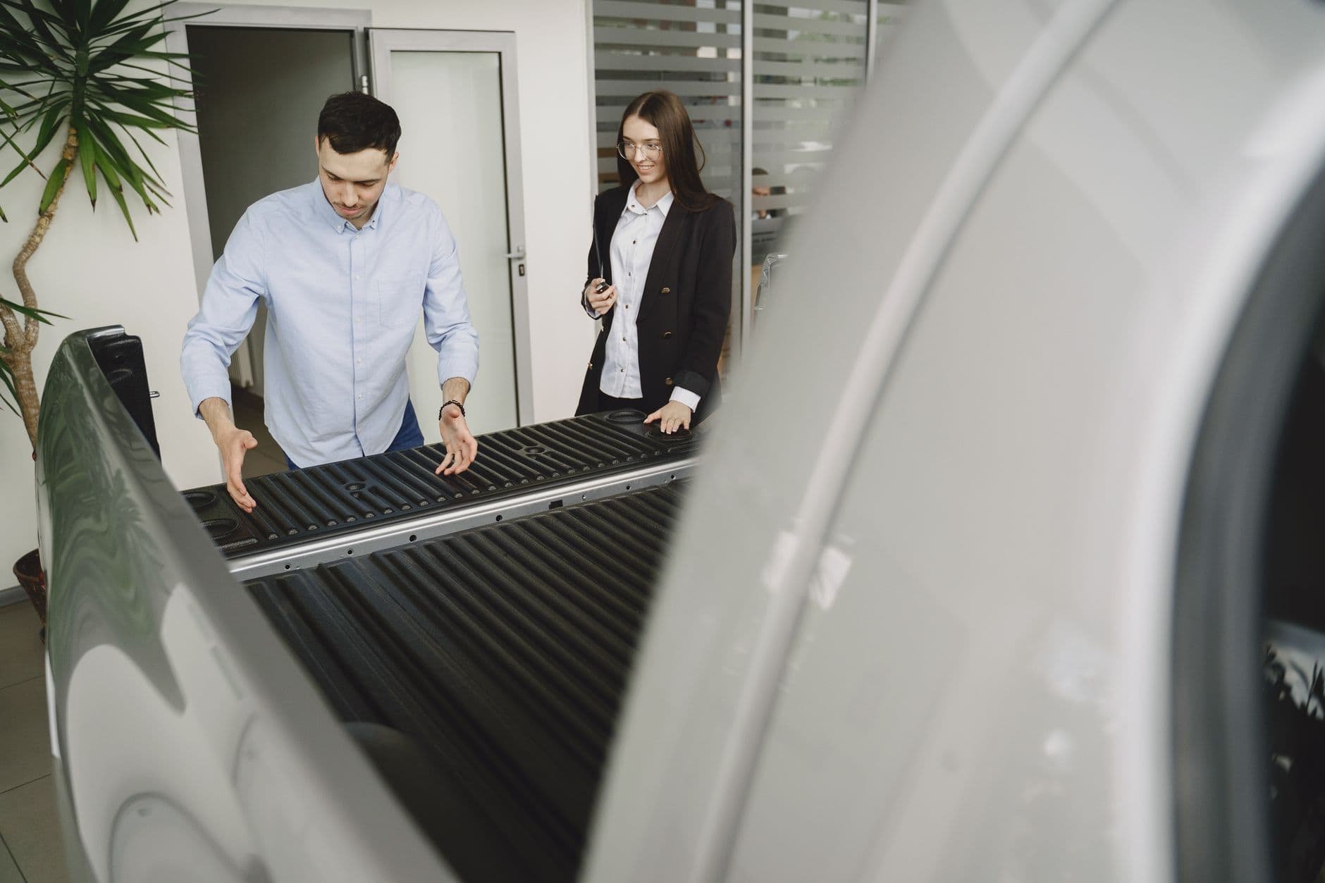 Salesman and client inspecting a pickup truck in a car dealership, discussing features.