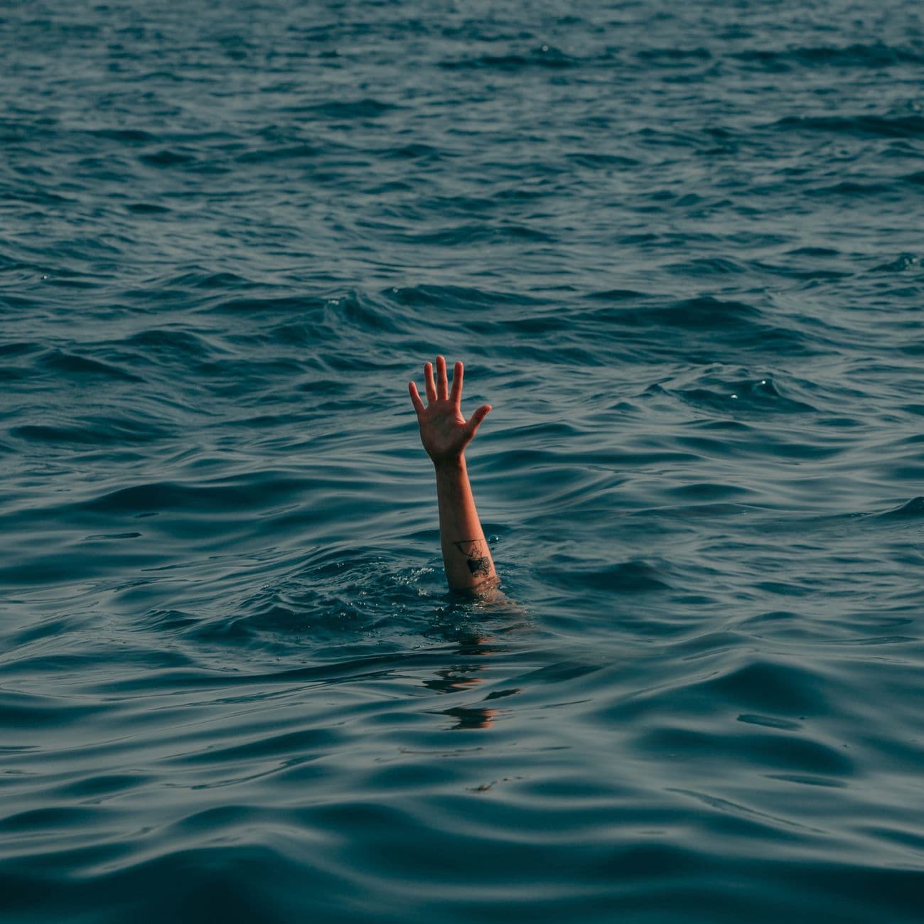 A lone hand emerges from the ocean, symbolizing distress and a call for help.