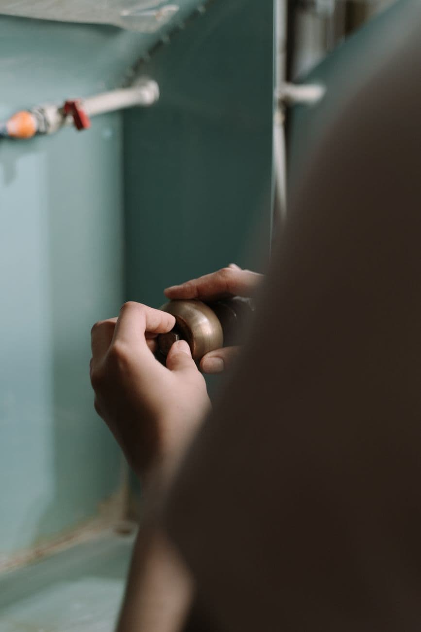 Close-up of hands adjusting a pipe under the kitchen sink, focusing on plumbing work.