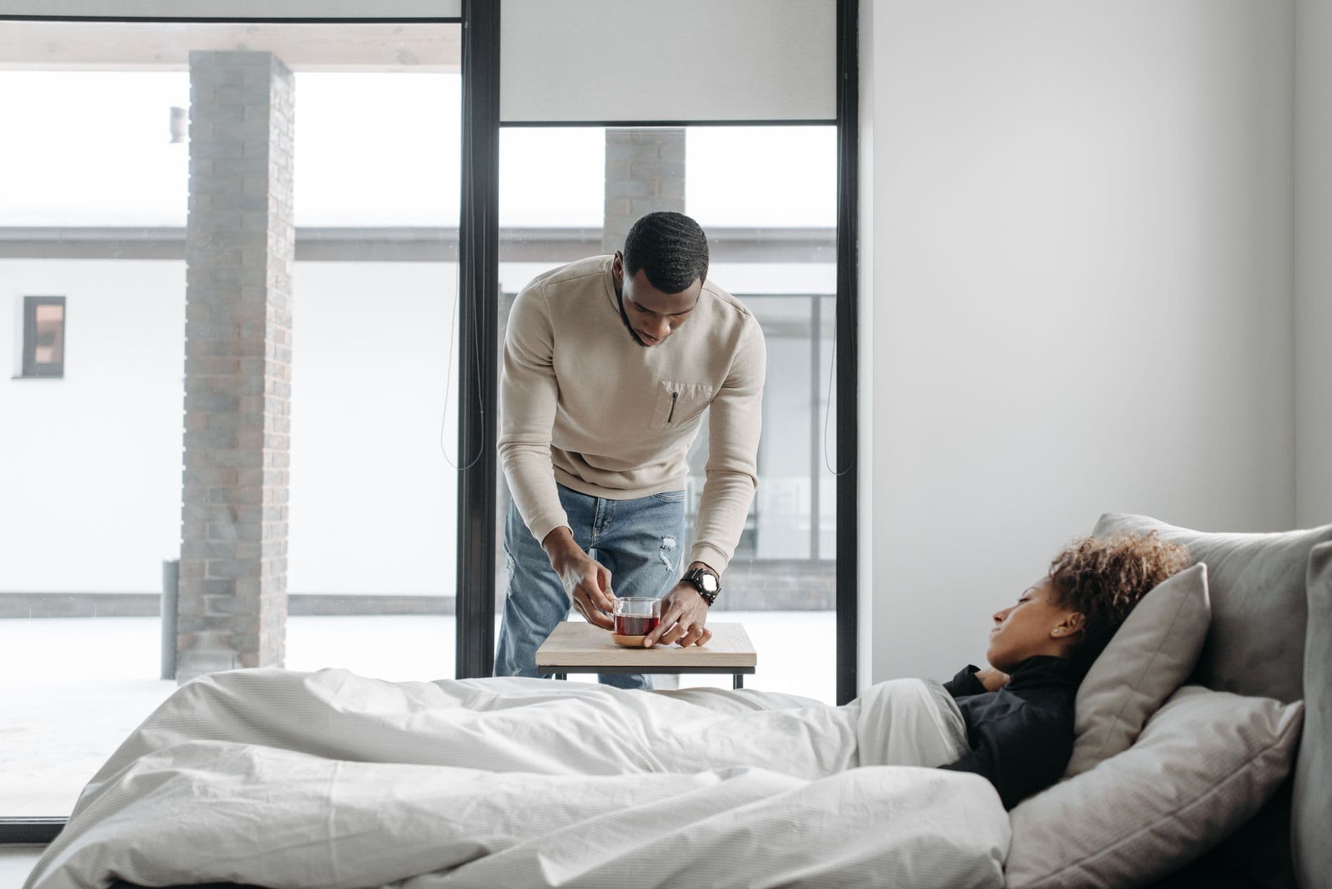 A man cares for his sick wife in bed, bringing her a cup of tea indoors.