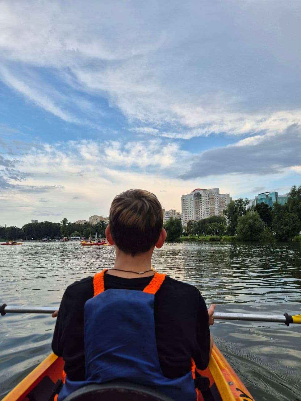 A person kayaking on a calm lake with city skyline under a cloudy sky at daytime.