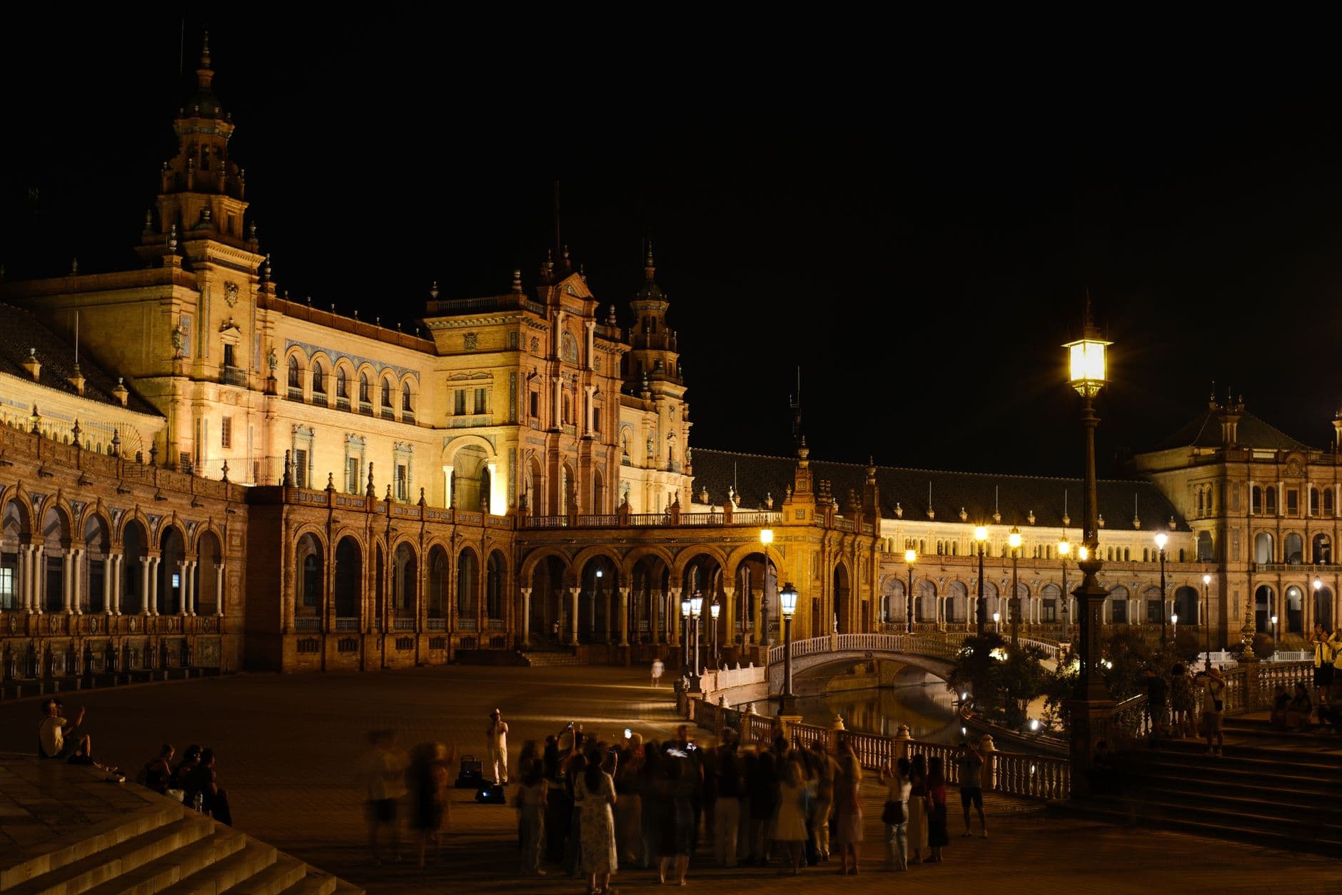 Stunning night view of Plaza de España in Seville, showcasing its ornate architecture and lively atmosphere.