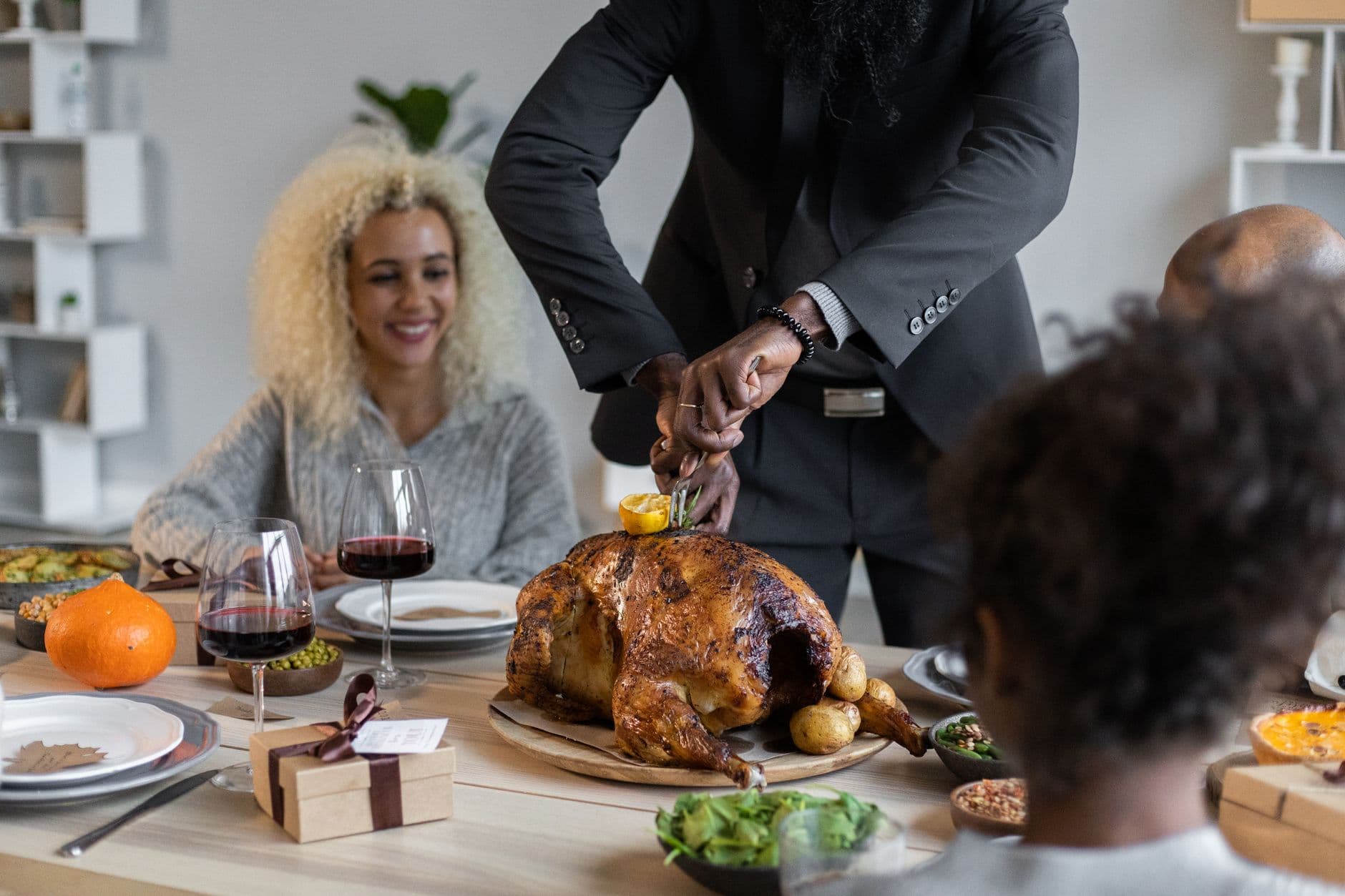 Crop anonymous African American male cutting roasted turkey with knife and fork while having Thanksgiving dinner with diverse guests