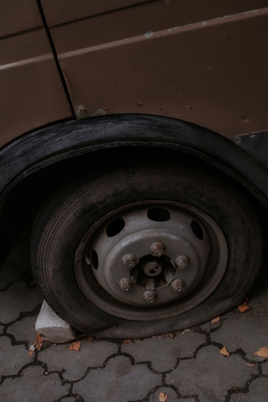 Detailed view of a flat tire on a car parked on a paved surface outdoors.