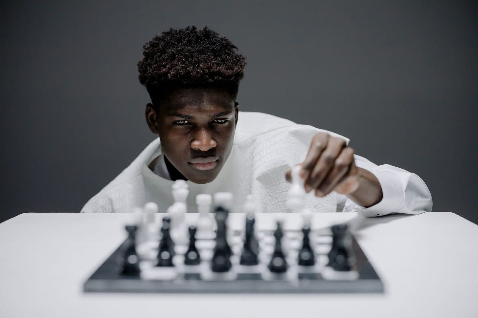 Young man in white playing chess indoors, demonstrating concentration and strategy.