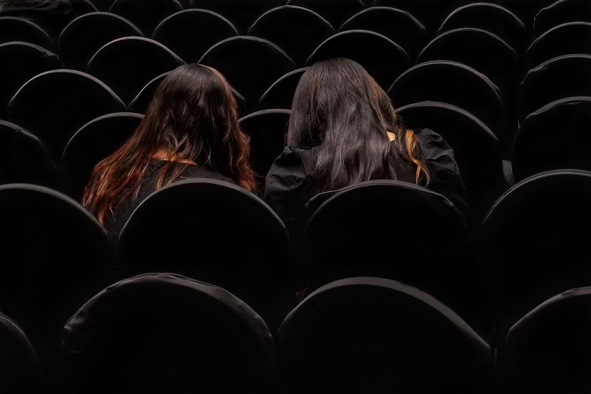 Two women seated in a dark theater, viewed from behind in Kolkata.