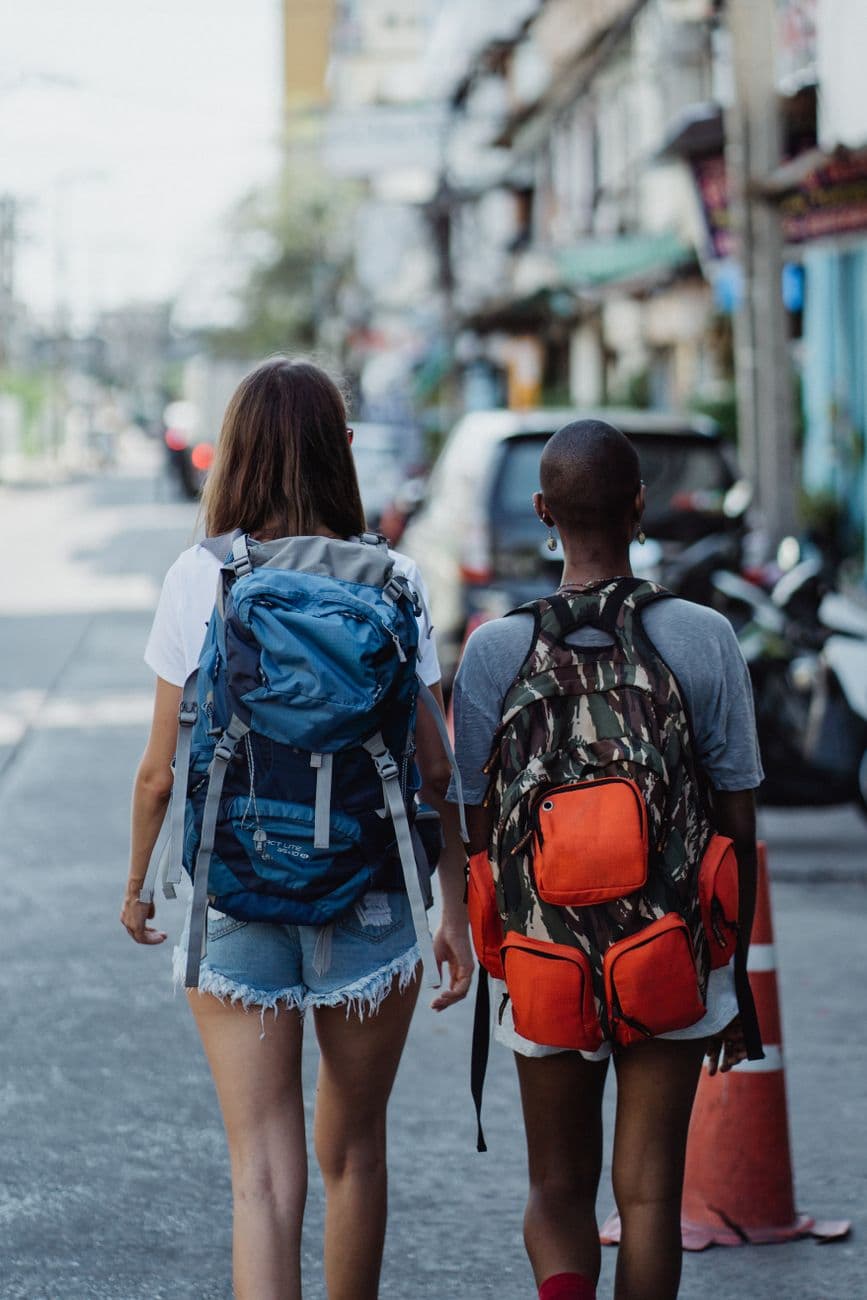 Two women with backpacks walk through an urban street, capturing the spirit of adventure and exploration.