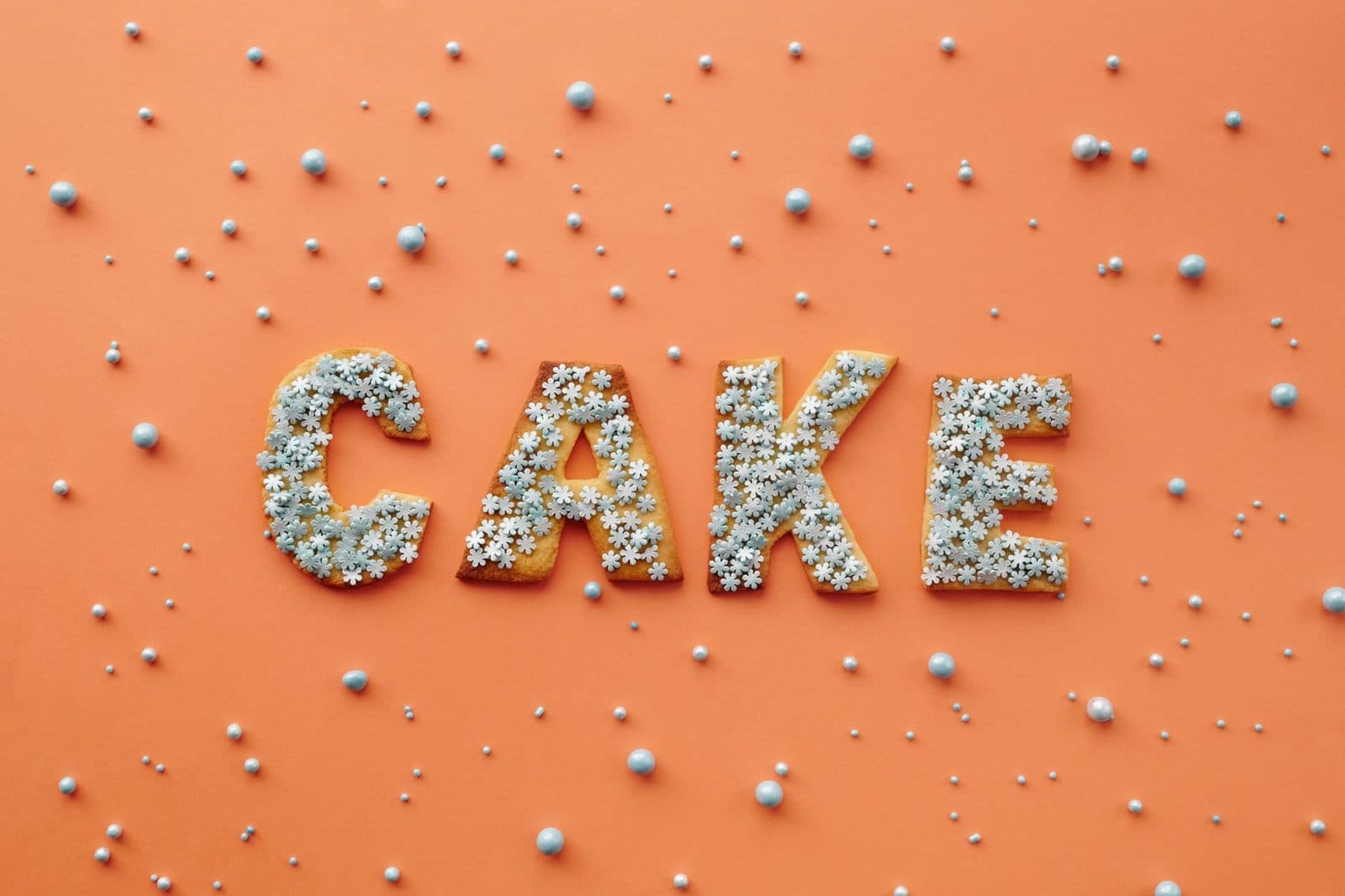 Flat lay of cake letters with sprinkles on orange background, perfect for celebrations.