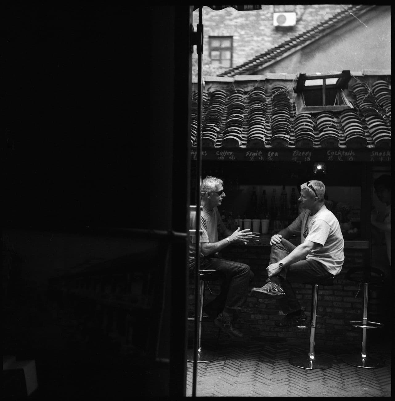 Two men enjoying a conversation at an outdoor bar, captured in black and white.