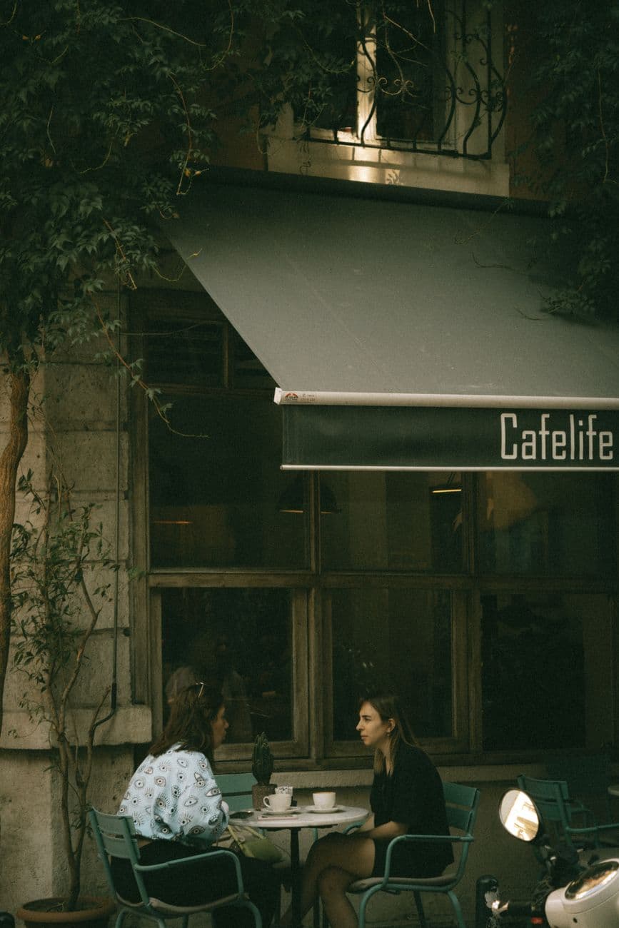 Two women enjoy a conversation at an intimate outdoor café setting, creating a cozy atmosphere.