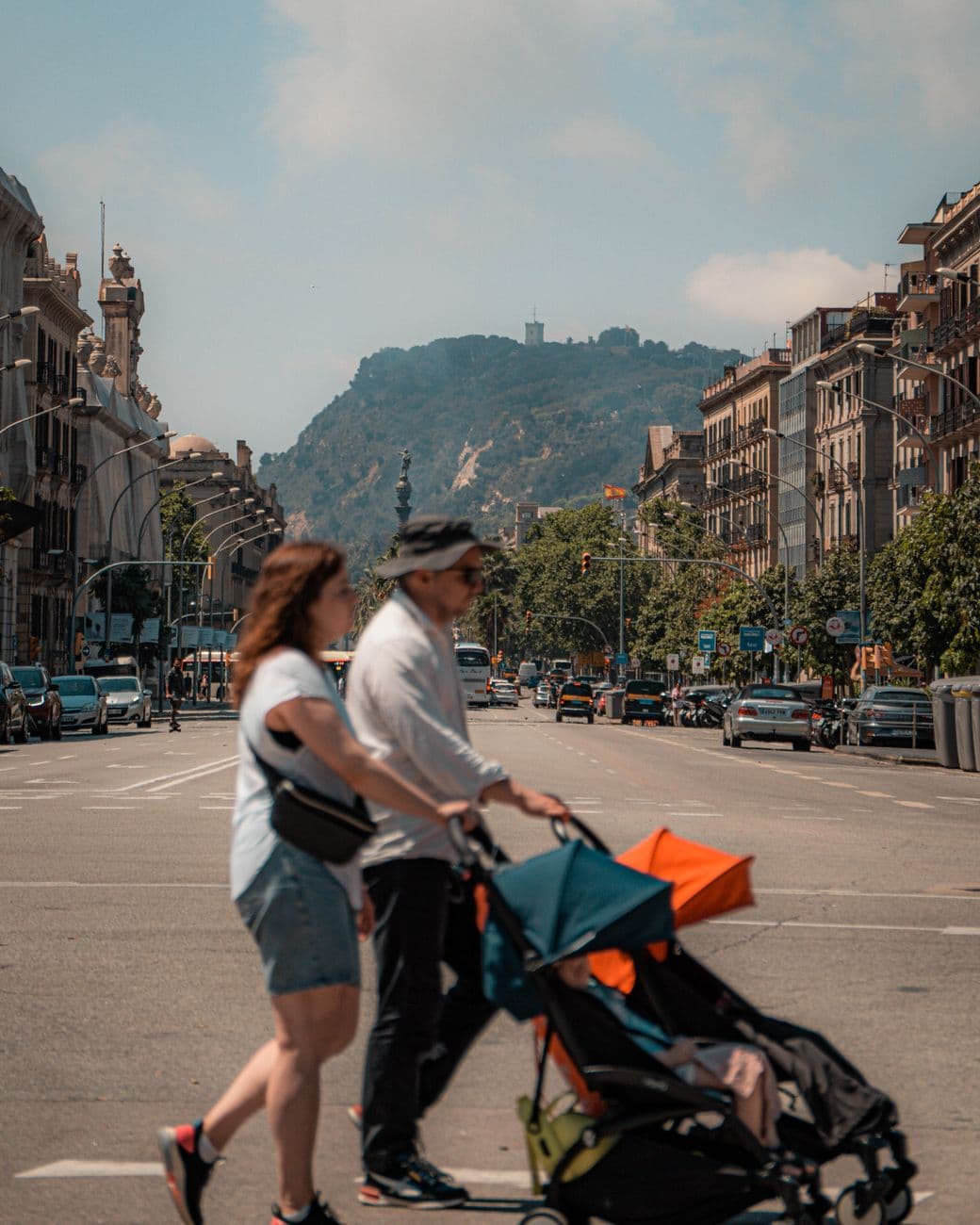 A family crossing a busy street in Barcelona with the cityscape and a stroller in view.