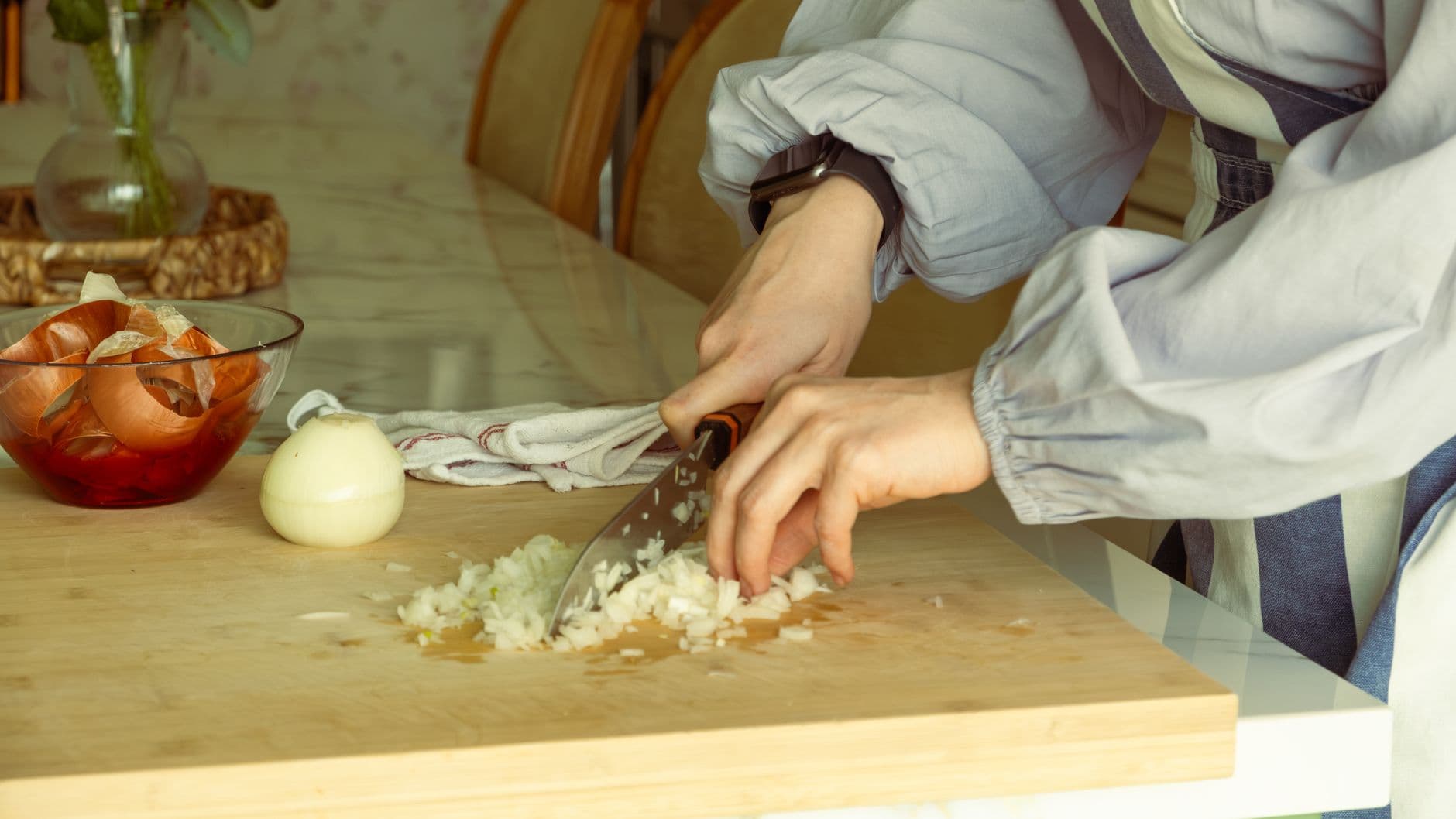 Close-up of onions being chopped on a wooden board in a kitchen setting.