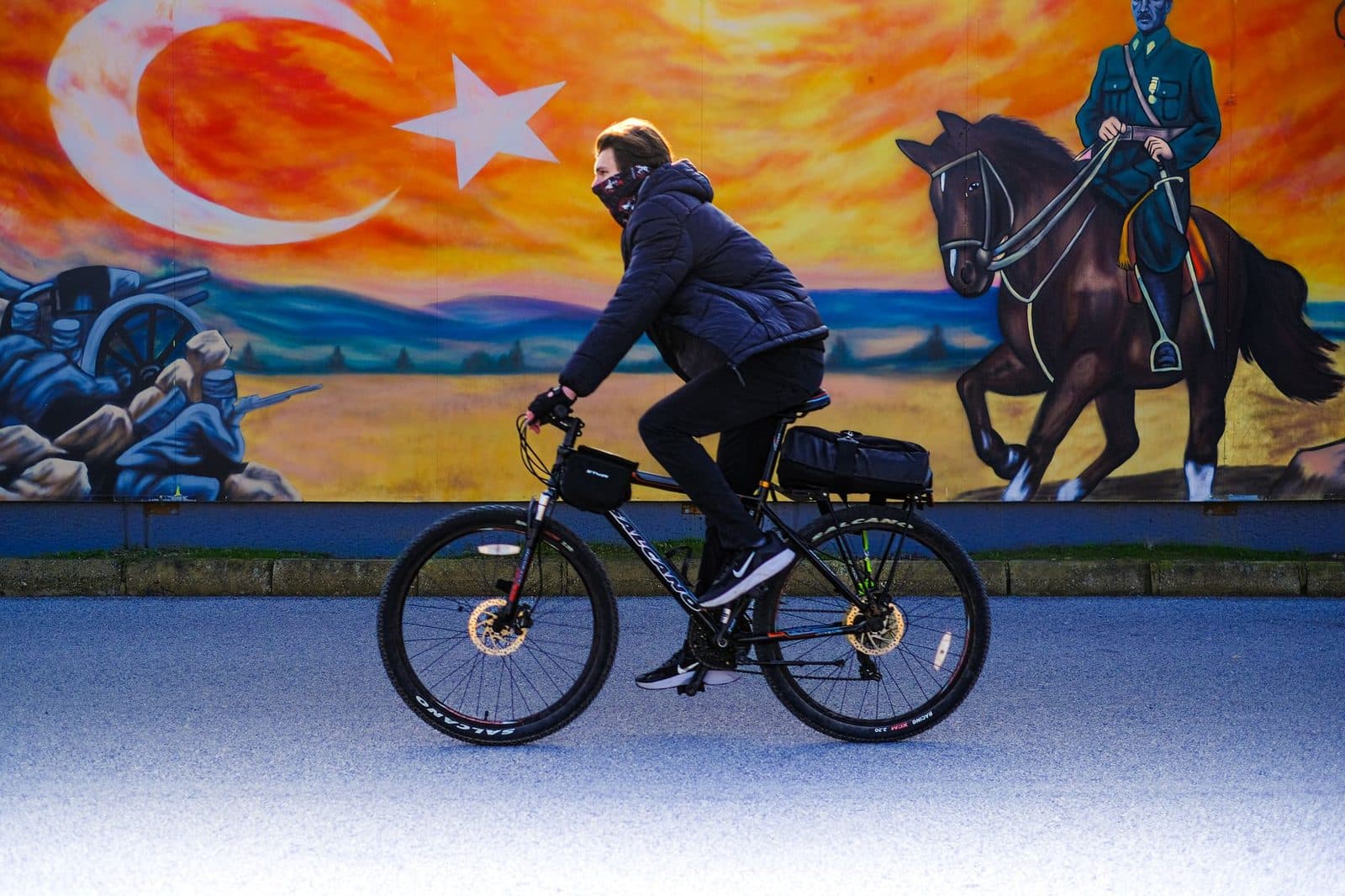 A cyclist rides by a mural featuring a horseman and the Turkish flag in bright colors.