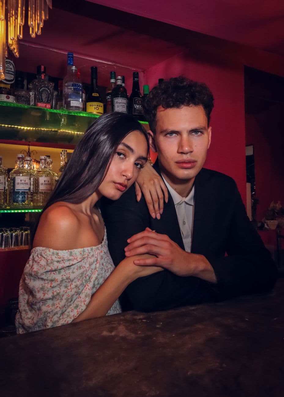 A fashionable couple sitting at a bar counter during a vibrant nightlife scene.