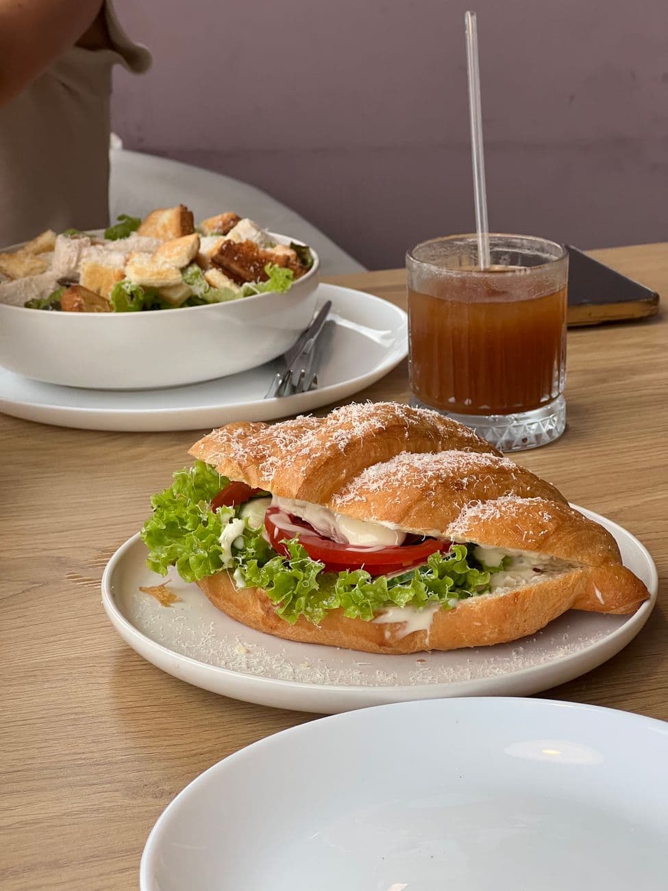 Delicious croissant sandwich with salad and iced tea on a wooden table. Perfect for a casual meal.