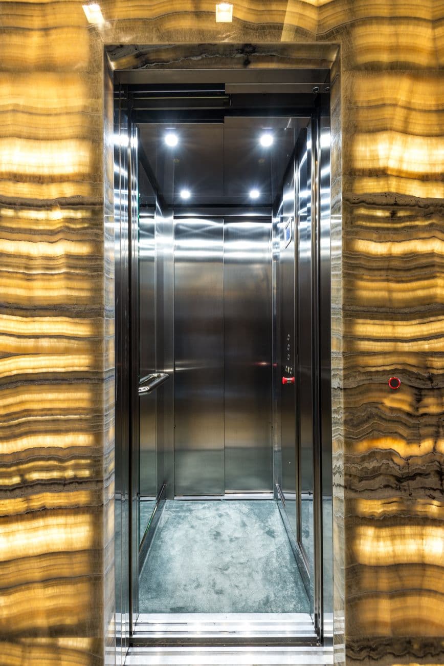 Brightly lit stainless steel elevator with marble walls and modern lighting design.