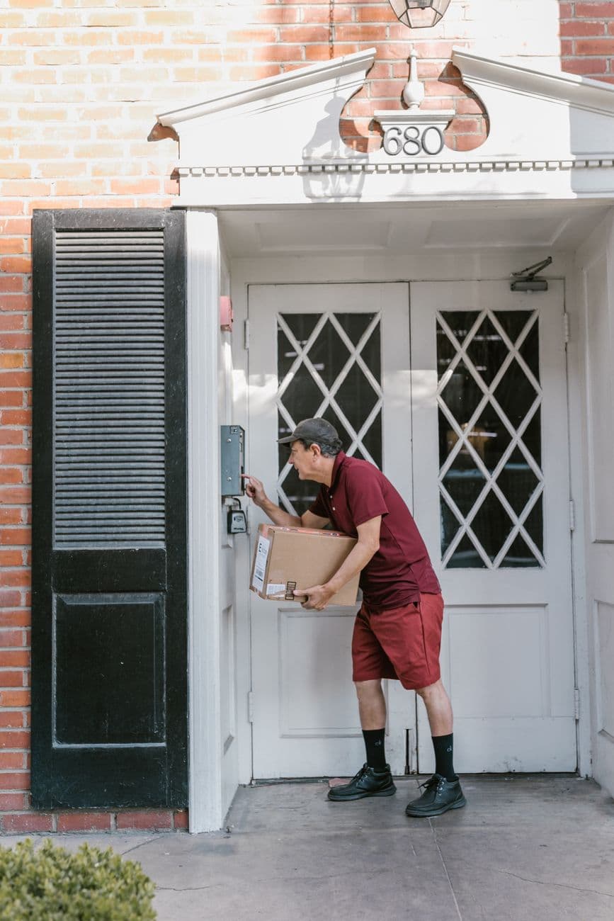 A courier in uniform delivers a package at a residential entrance, ringing the doorbell.