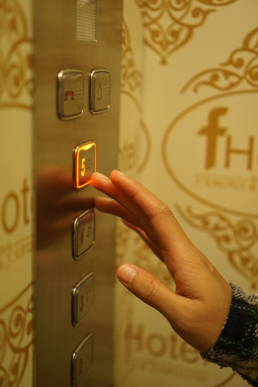 A hand pressing the fifth-floor button inside a hotel elevator with elegant decor.