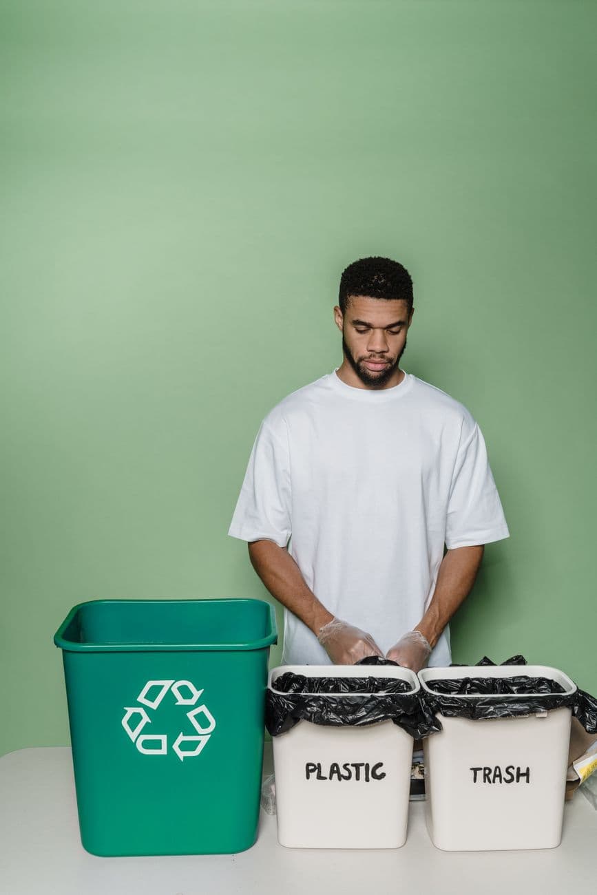 Man in studio sorting recyclable plastic and trash into bins, promoting sustainability.