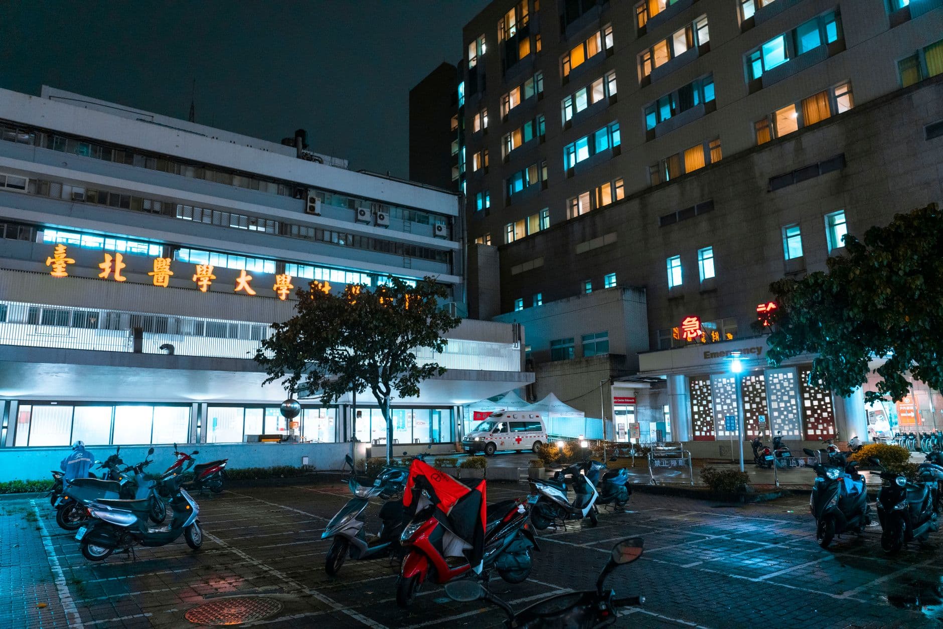 Night view of a hospital with scooters parked outside, illuminated by bright city lights.