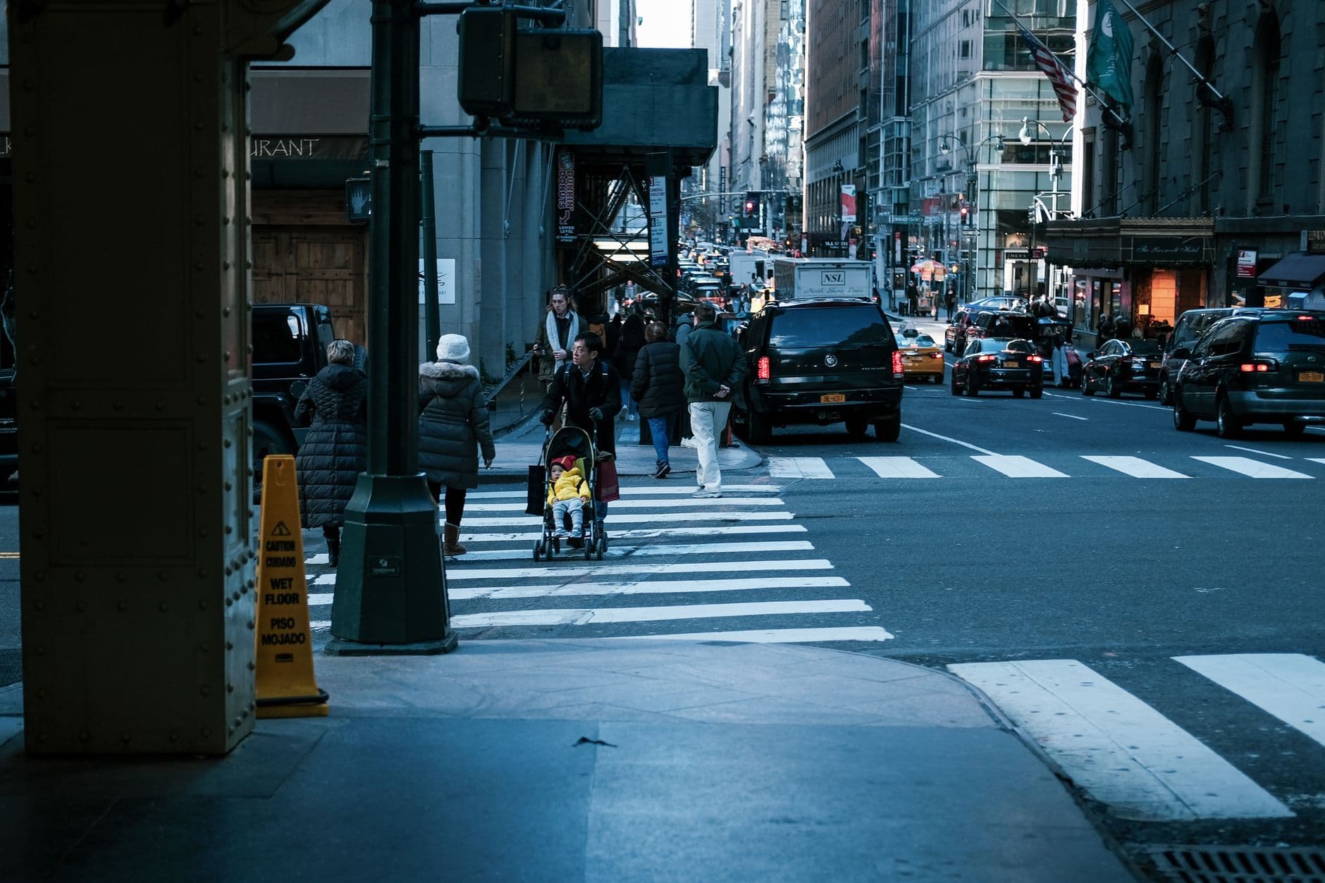 Urban street scene with people crossing a vibrant city street surrounded by tall buildings and numerous vehicles.