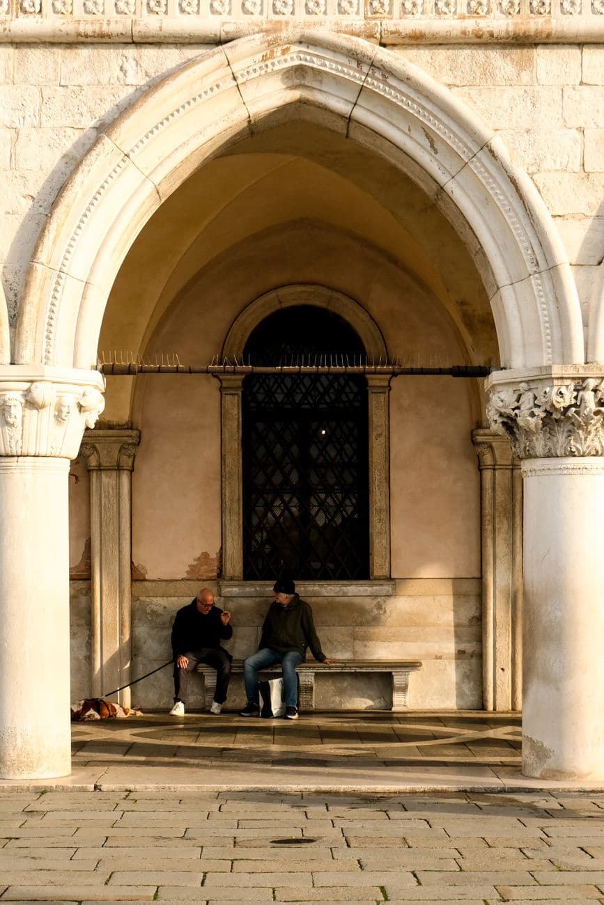 Casual conversation under a historic Venetian arch, capturing elements of classic architecture and daily life.