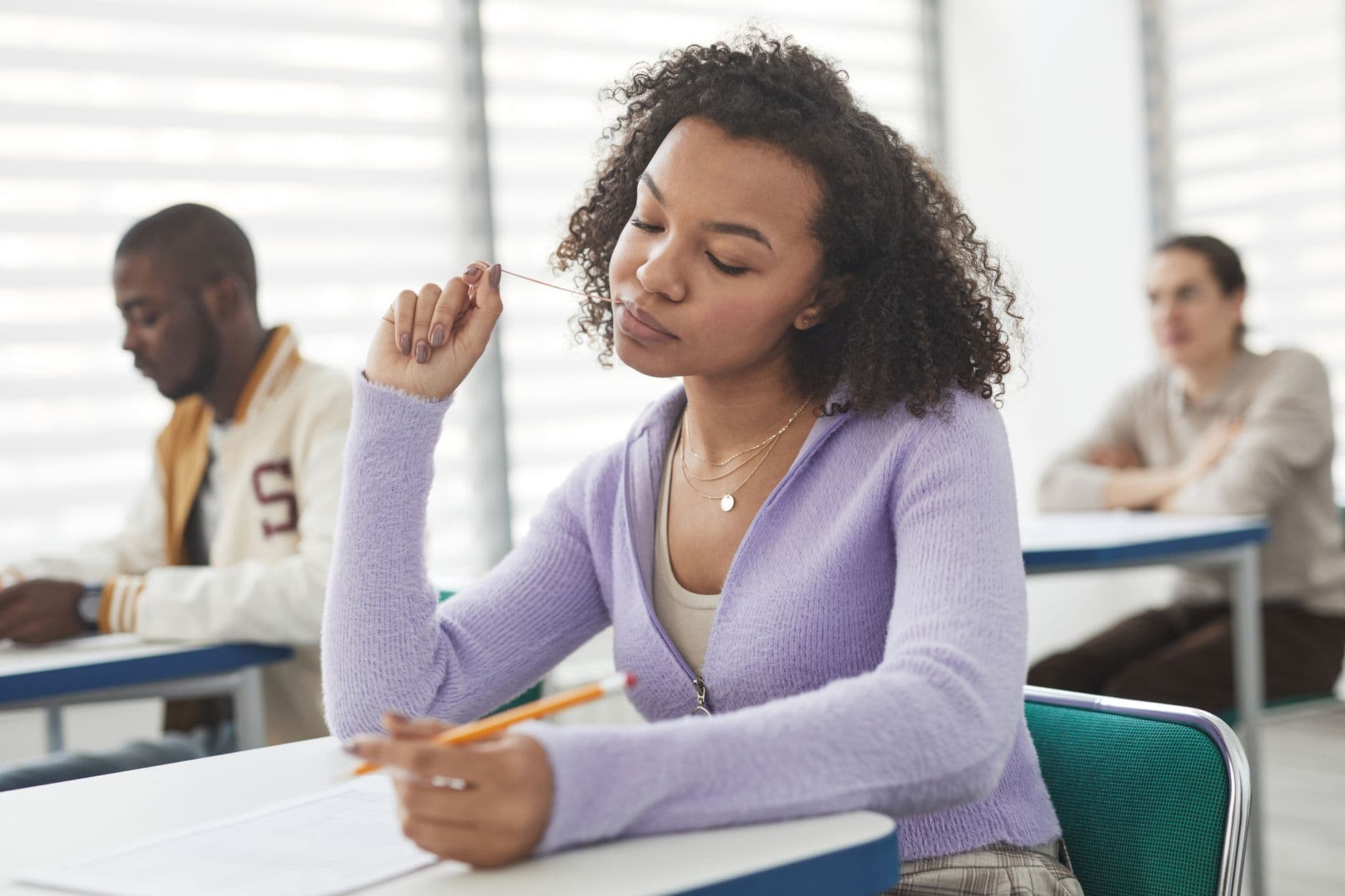 A female student concentrating on a test in a brightly lit classroom.