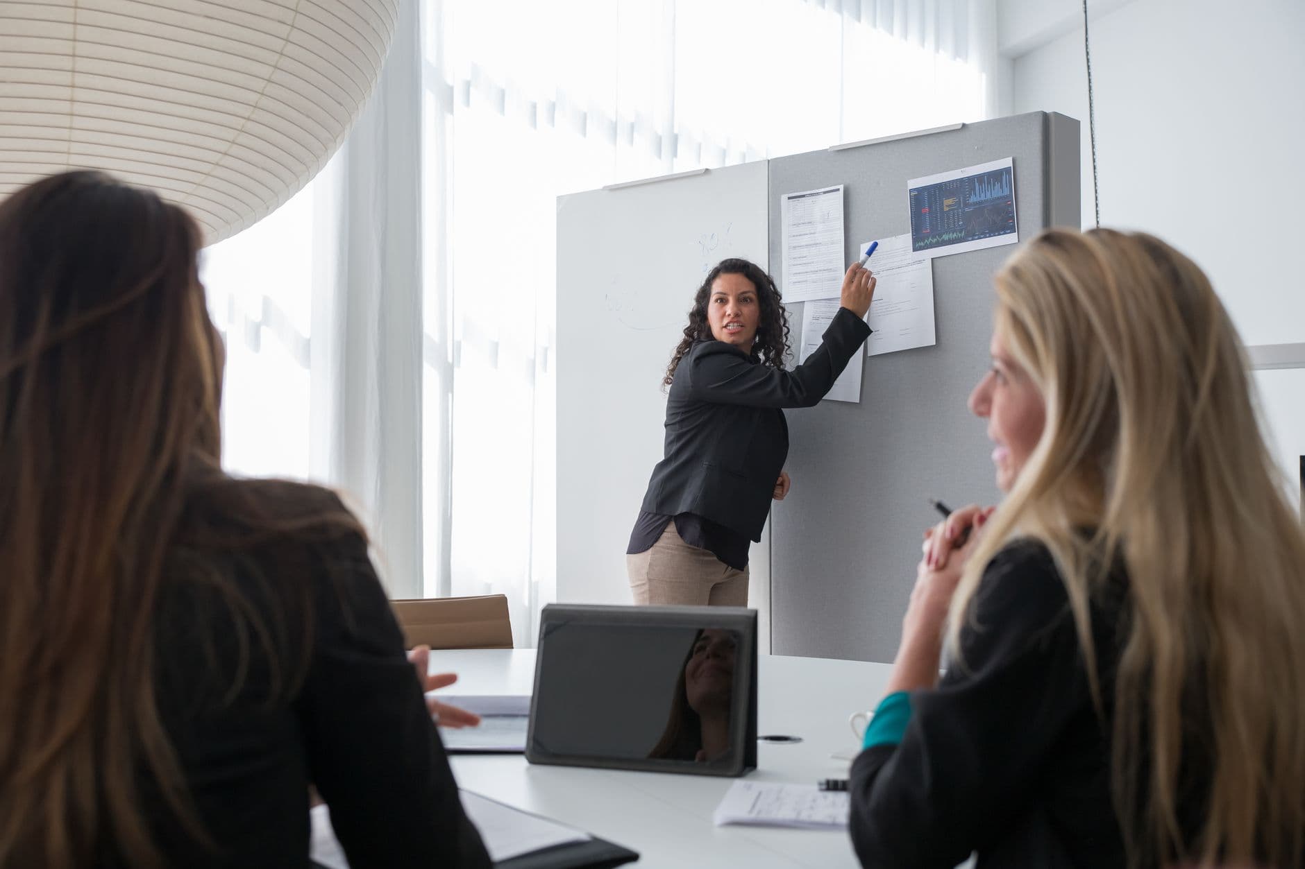 Professional woman presenting data on a whiteboard to colleagues in a bright office environment.