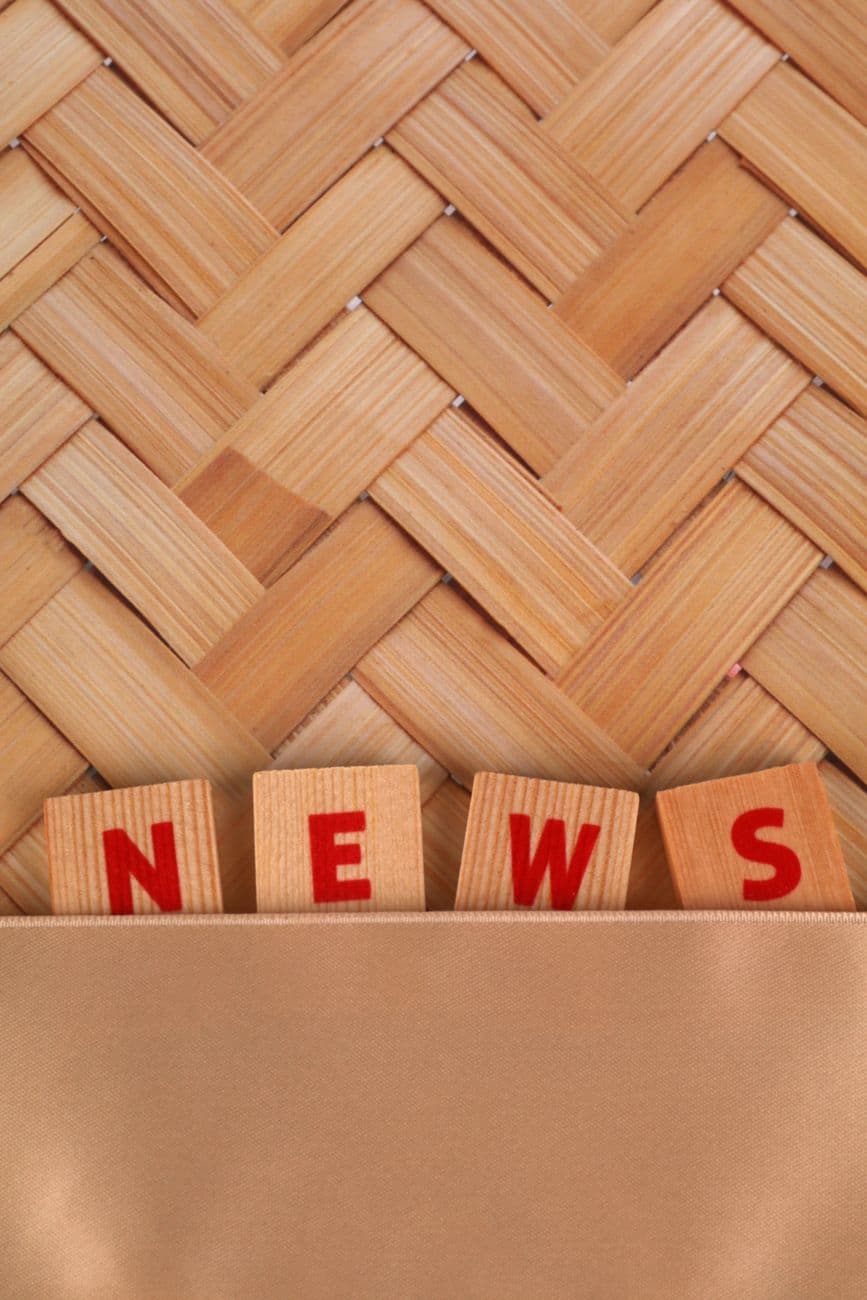 Close-up of wooden blocks spelling 'NEWS' against a woven wooden background.