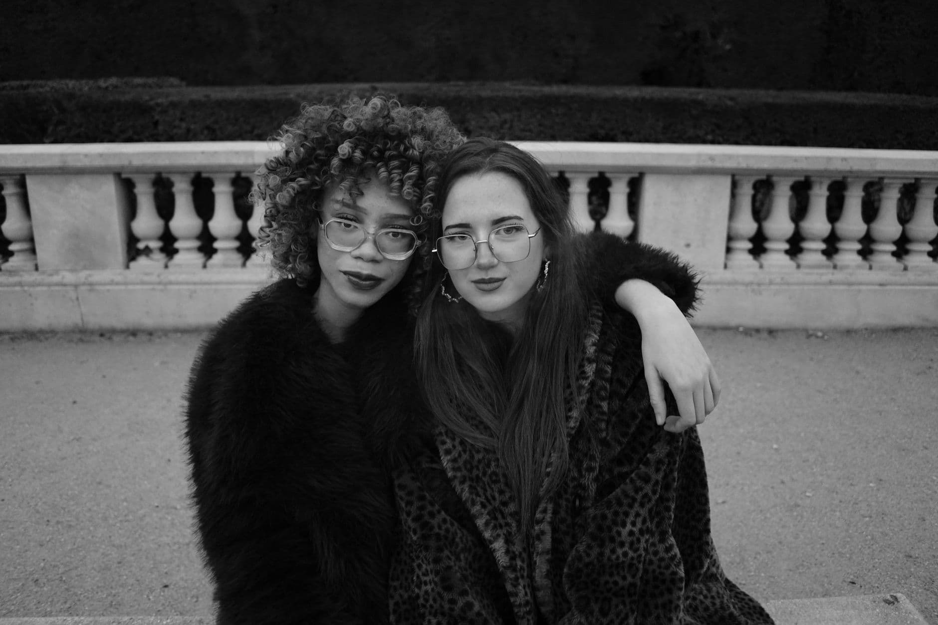 Two stylish friends in fashionable coats in black and white outdoor setting.