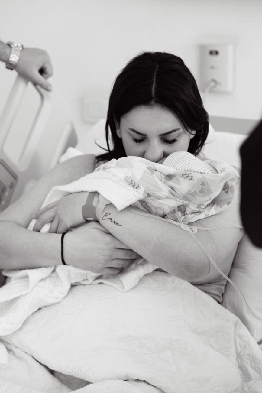 A touching black and white photo of a mother lovingly holding her newborn in a hospital bed.