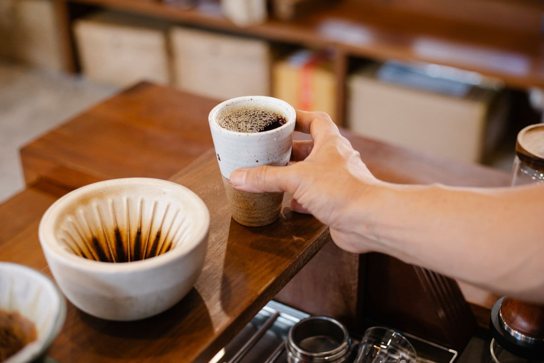 Coffee being served in a ceramic cup over a wooden countertop with ceramic brewing equipment nearby.