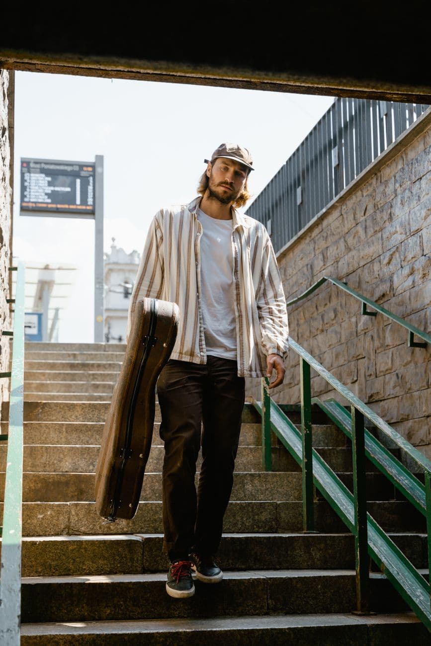 Man carrying guitar case while walking down outdoor stairs during the day.