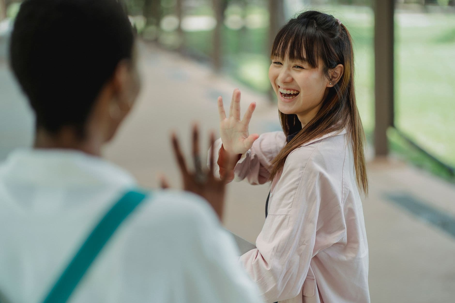 Young cheerful best multiethnic friends waving hands while saying hello to each other on pavement