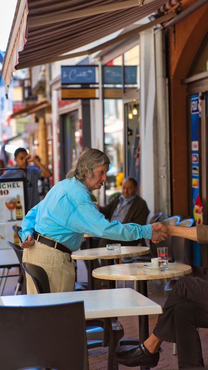 Two adults casually shaking hands at an outdoor café, showcasing urban street life.