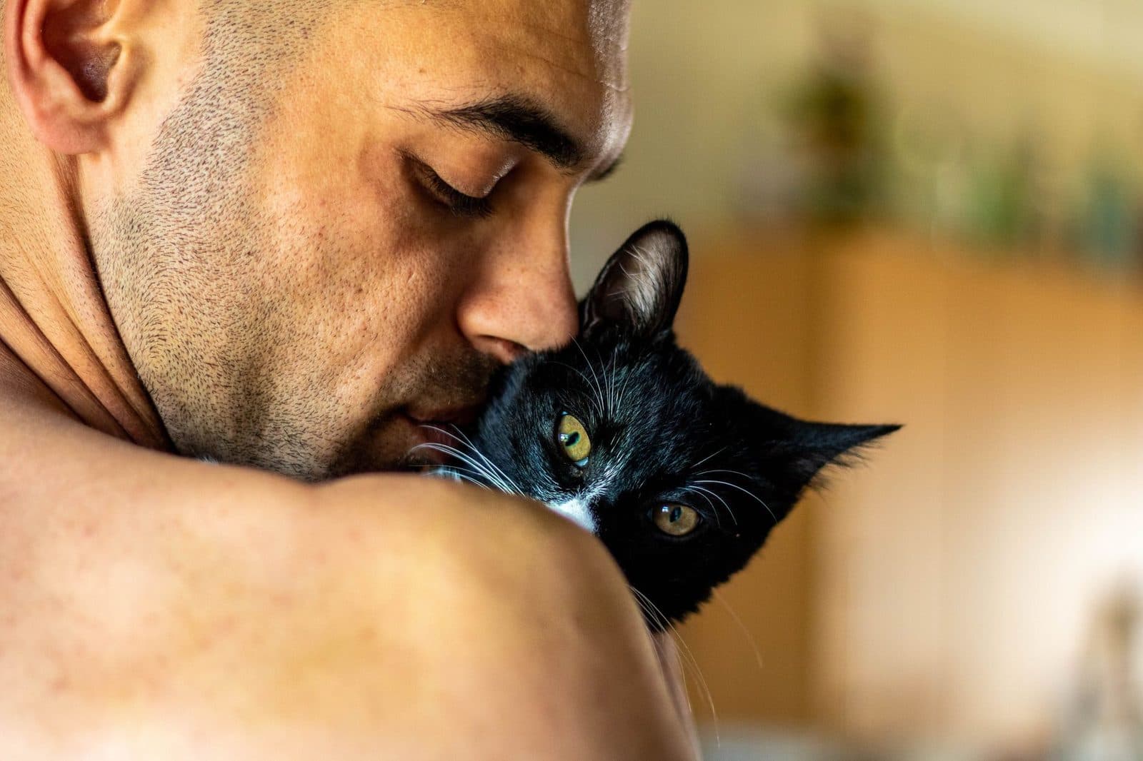 A close-up of a man affectionately holding a black and white cat in a warm home setting.